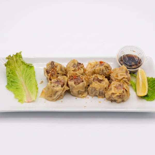 A plate of steamed dumplings with lettuce, lemon, and a side of soy sauce.