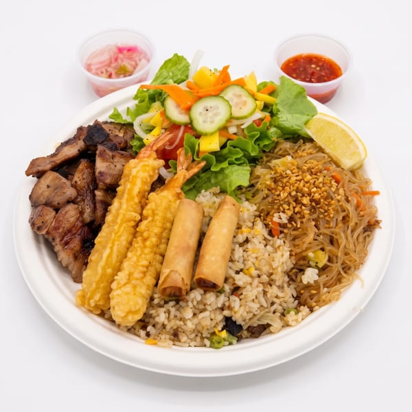 A large plate of Filipino food with grilled pork, fried shrimp, spring rolls, rice, noodles, and salad.