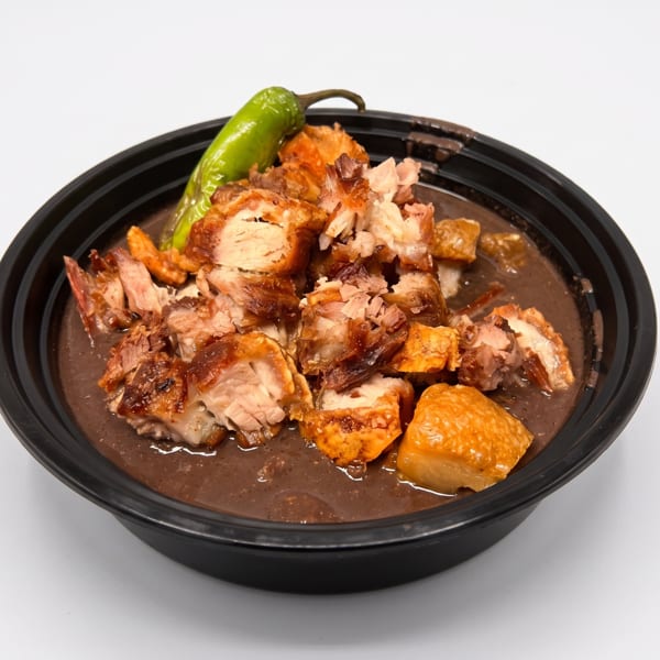 Crispy pork belly with a green chili pepper in a dark sauce, served in a black bowl.